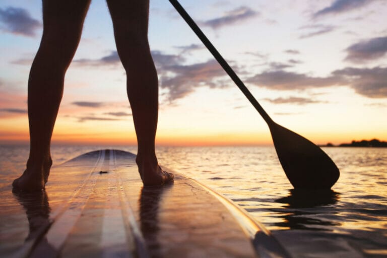 stand up paddle board on the beach, close up of standing legs and paddle
