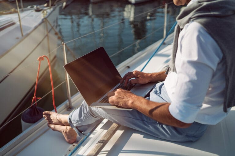 Senior man is working with his laptop on the deck of a sailboat