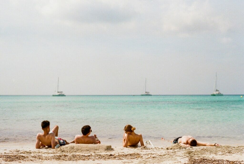 four people relaxing at the beach with view on the ocean and three yachts in the distance