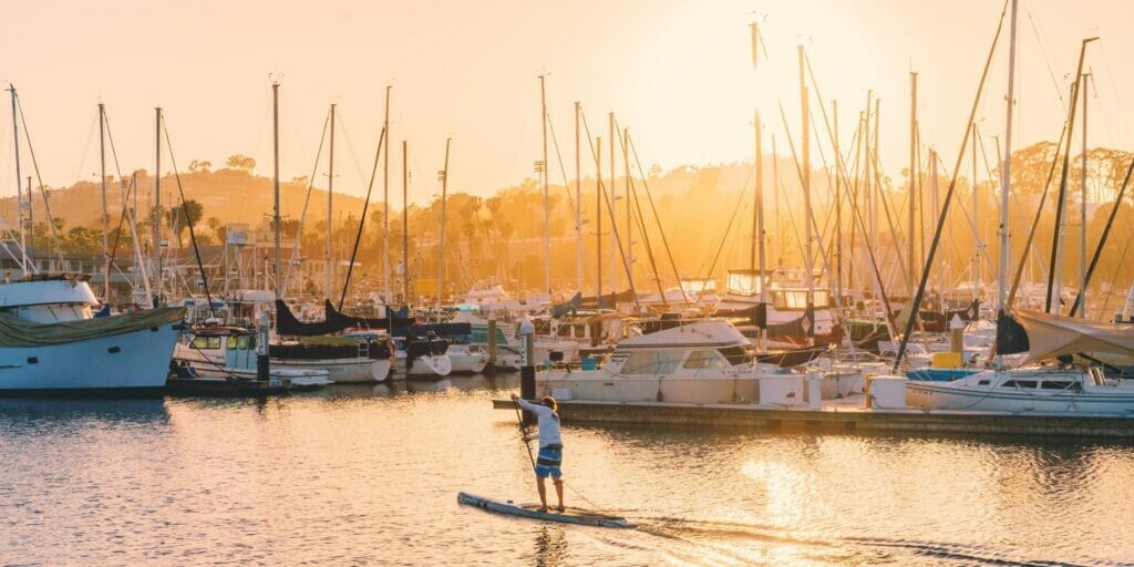 Man on SUP board paddling through marina during sunset