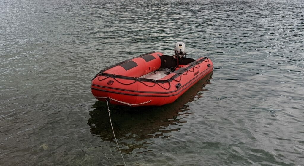 small red soft inflatable boat with tiller steering floating on calm water