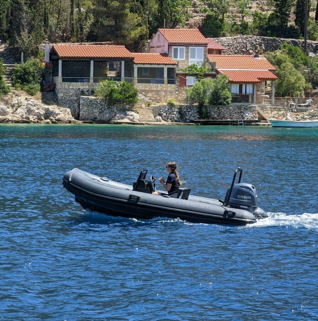 young girl driving a RIB (rigid inflatable boat) in the Dalmatian sea. In the background you see a beautiful waterfront house