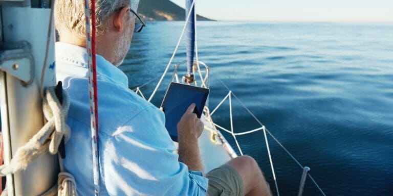 Man using a tablet computer while sitting on the bow of a sailboat