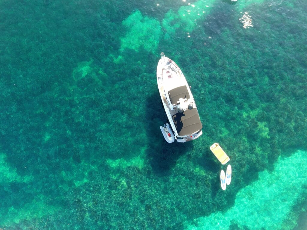 Aerial view of a Nordhavn N43 black swan anchored in a shallow bay with crystal clear water.
